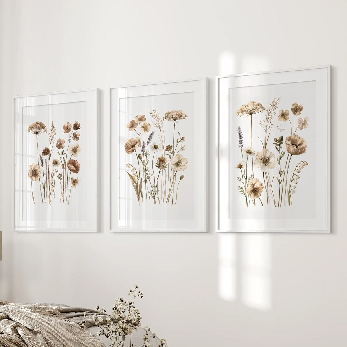 Neutral wildflower wall art in three white frames with mats beside a bed.