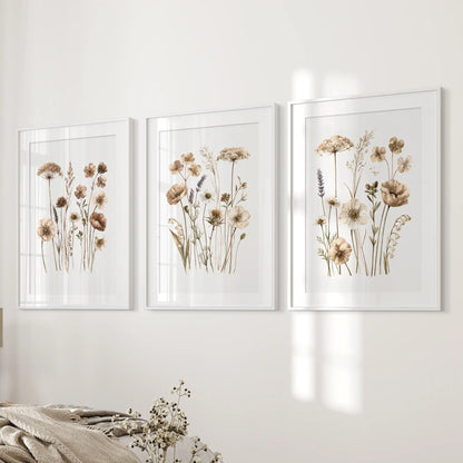 Neutral wildflower wall art in three white frames with mats beside a bed.