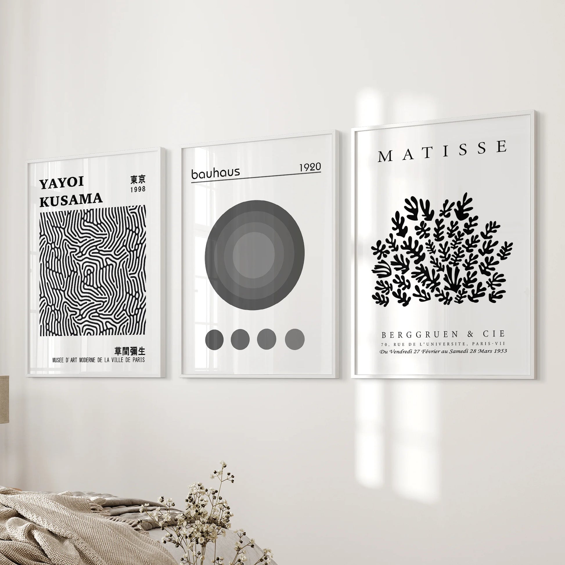 Three white-framed geometric posters bring crisp Bauhaus balance to the bedroom wall beside the bed, adding sharp modern detail.